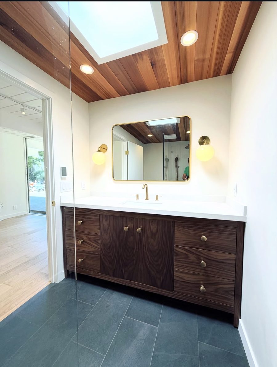 Bathroom vanity after remodel — walnut cabinetry, brass fixtures, and skylight