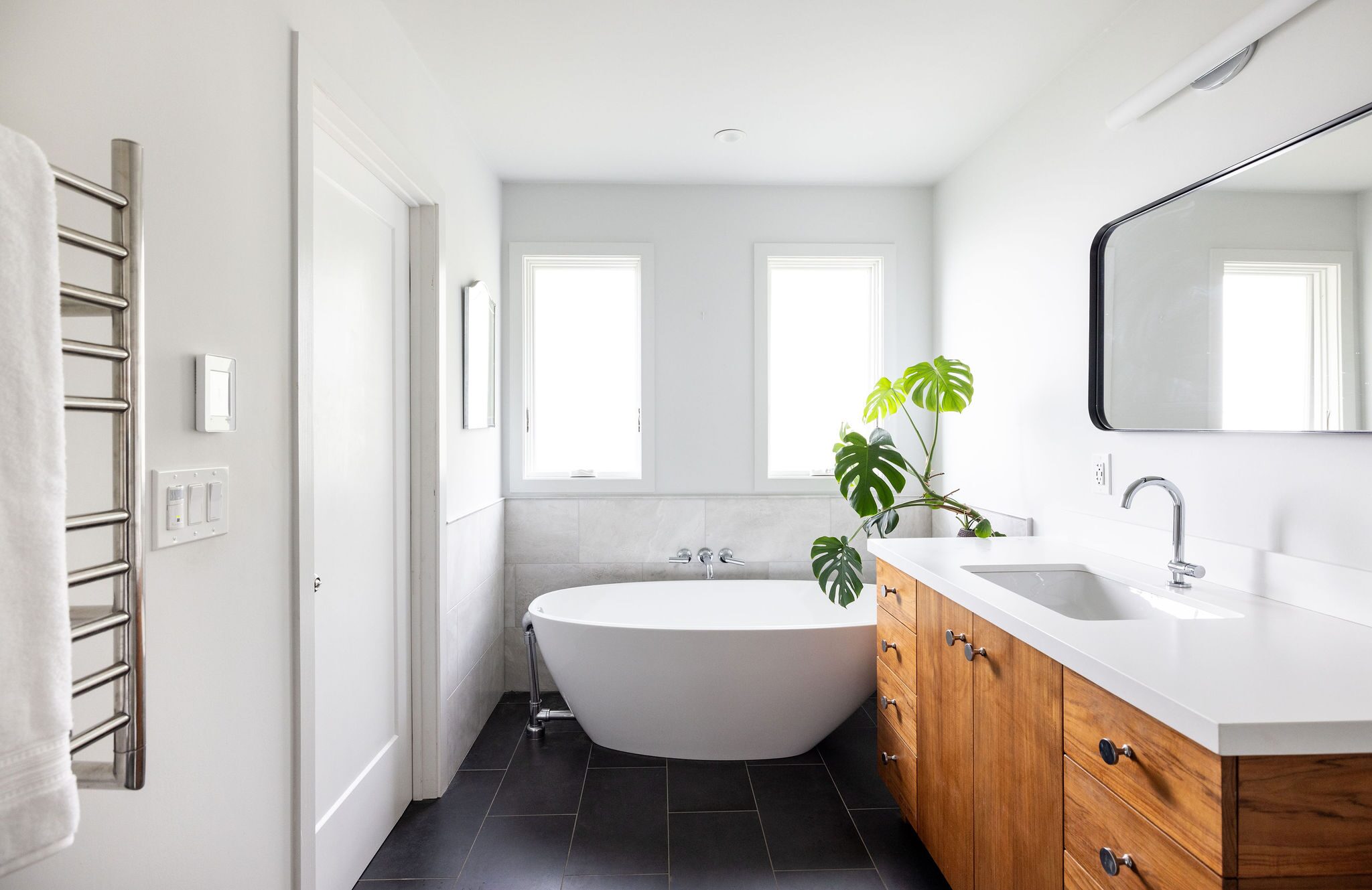 Freestanding soaking tub with custom walnut vanity and monstera plant in a Build Shepherd bathroom remodel in Marin County, CA